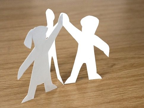 Drei ausgeschnittene Papierfiguren halten sich an den Händen auf einem Holztisch.