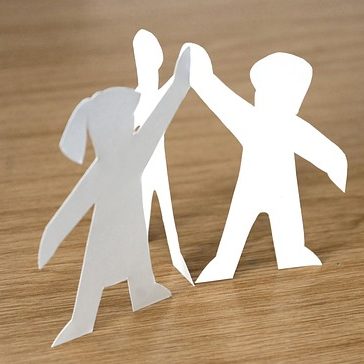 Drei ausgeschnittene Figuren aus Papier, die sich an den Händen halten.