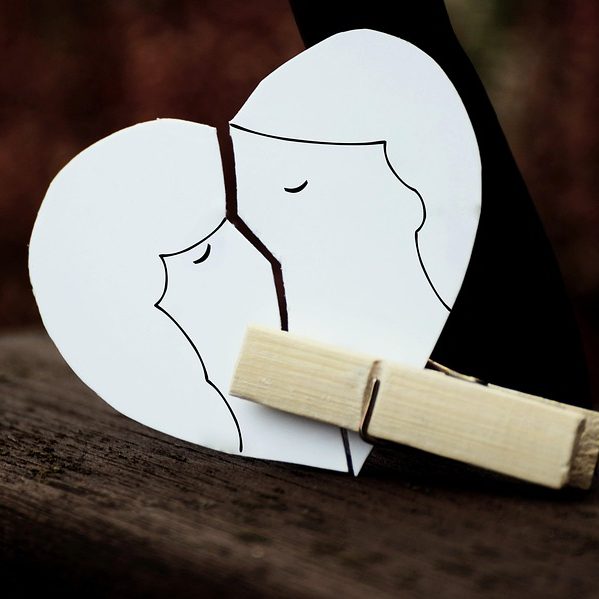 Papierherz mit zwei sich küssenden Silhouetten, gehalten von einer Wäscheklammer.