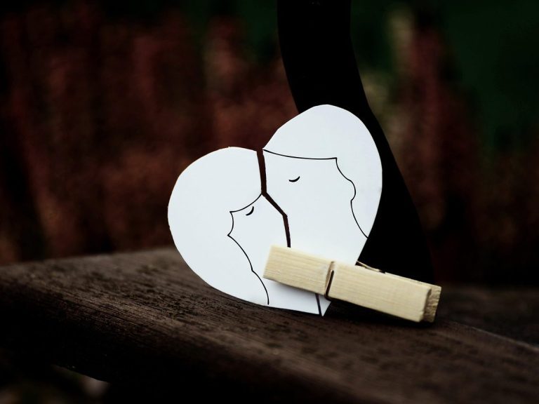 Zwei umarmende Köpfe in Form eines Herzens, gehalten von einer Wäscheklammer.