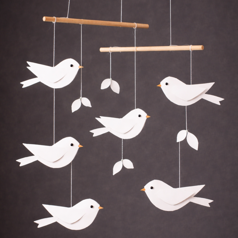 Hängemobil aus weißen Vögeln und Blättern auf dunklem Hintergrund.